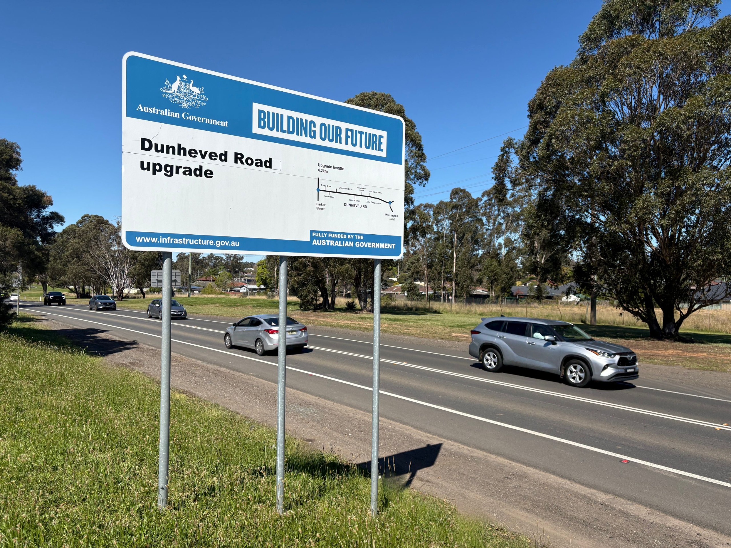 A sign of the Dunheved Road upgrade with the road in the background.
