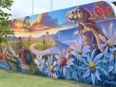 A large mural at Gipps Street Recreation Precinct depicts a vibrant landscape with native plants, flowers and wildlife, including a lizard and kangaroo, alongside a bicycle and young people walking and riding.